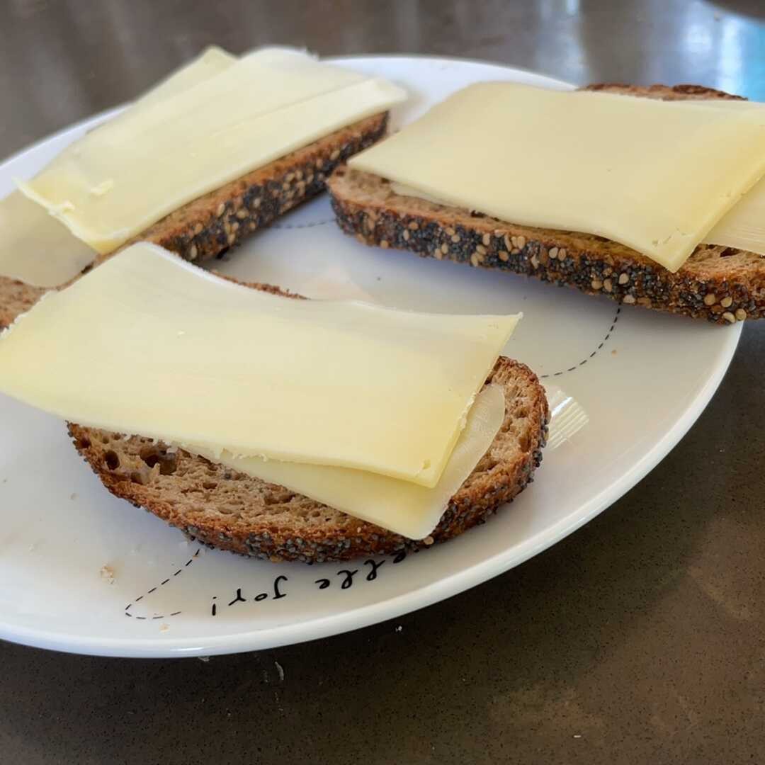 Three slices of bread with cheese on a plate. The bread is a "whole weat" type, with a crunchy crust and slightly dark in the middle. Some slices of cheese are put on the bread and that's it. No other ingredients are used.